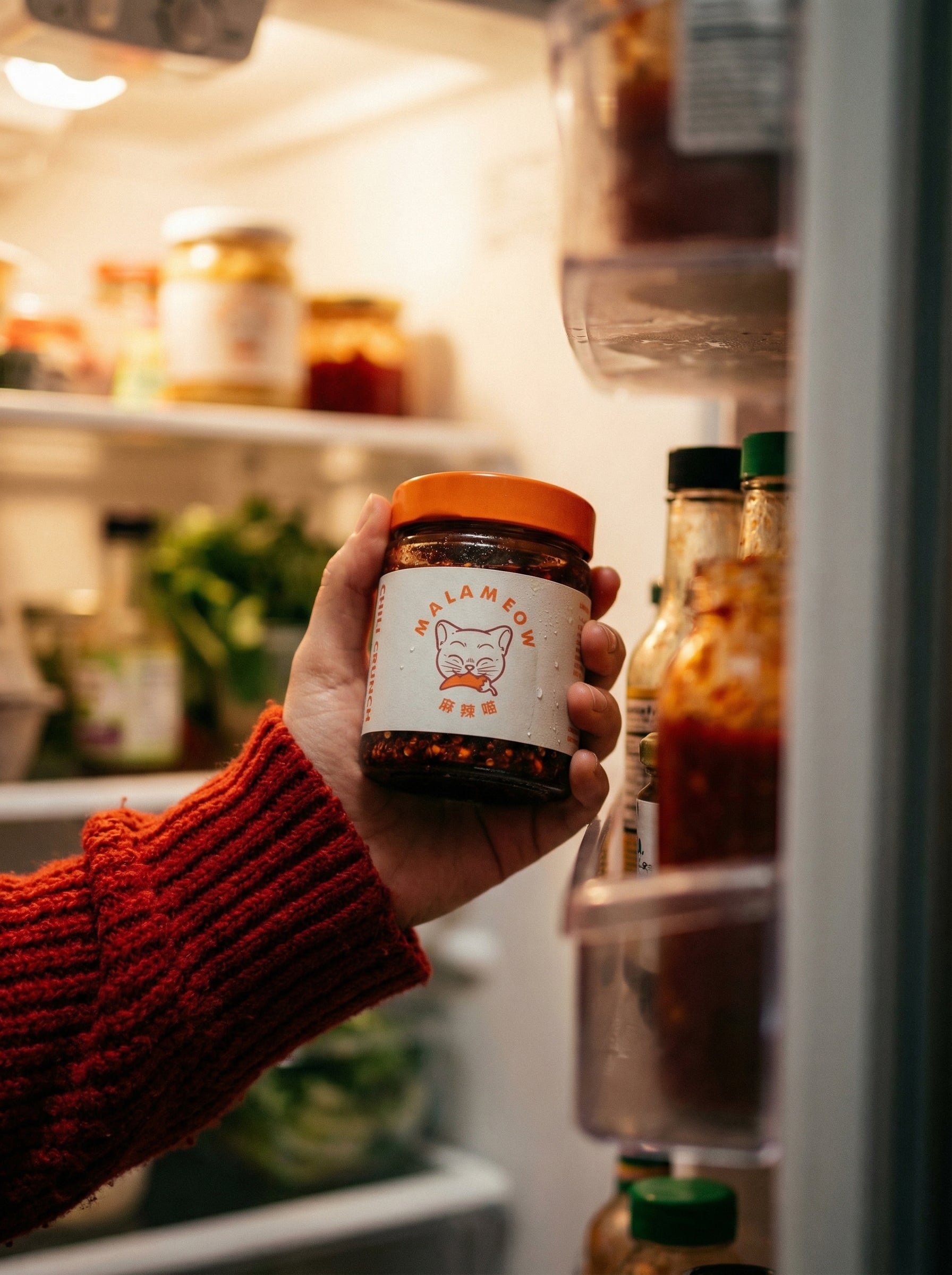 Hang holding a cold jar of MalaMeow Chilli Crunch out of the fridge
